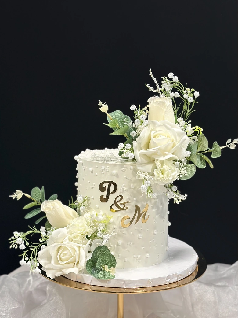 Ivory wedding cake with white rose arrangements on a consistent studio backdrop